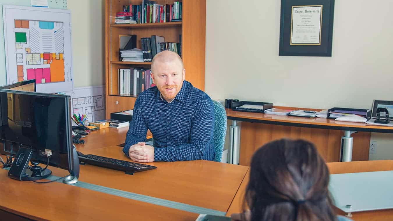 A pastor speaks with a visitor across the desk in his office within Regent's online PhD in Counseling and Psychological Studies – Pastoral Counseling program