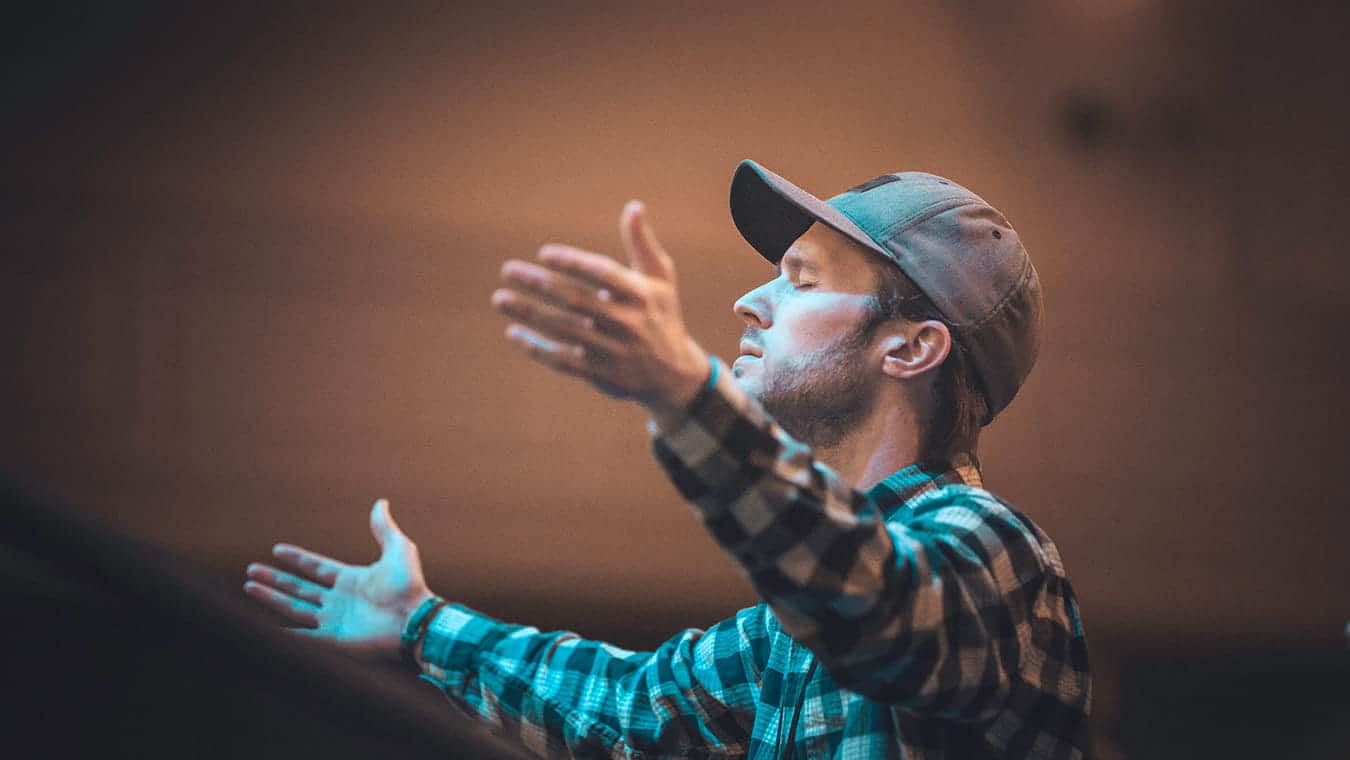 A graduate student worshipping with arms up in the chapel at Regent University as a part of the Master of Divinity in Theology & Ministry (M.Div.) in Worship and Media degree