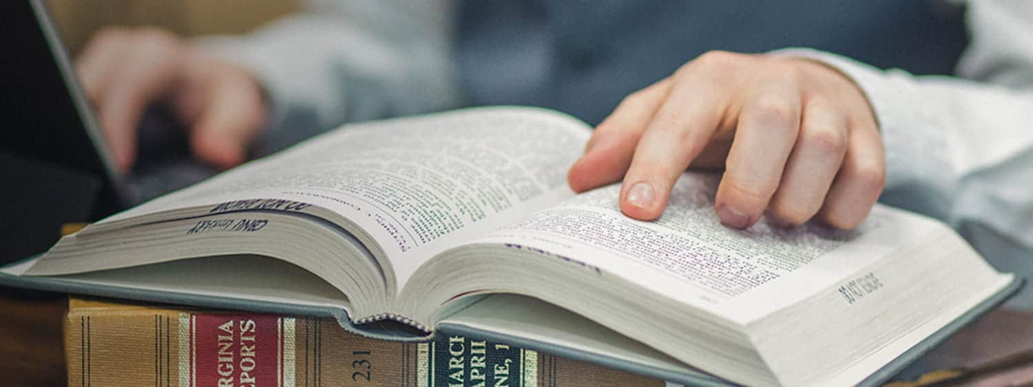 A student's finger pointing to text on an open book in the Regent University library.