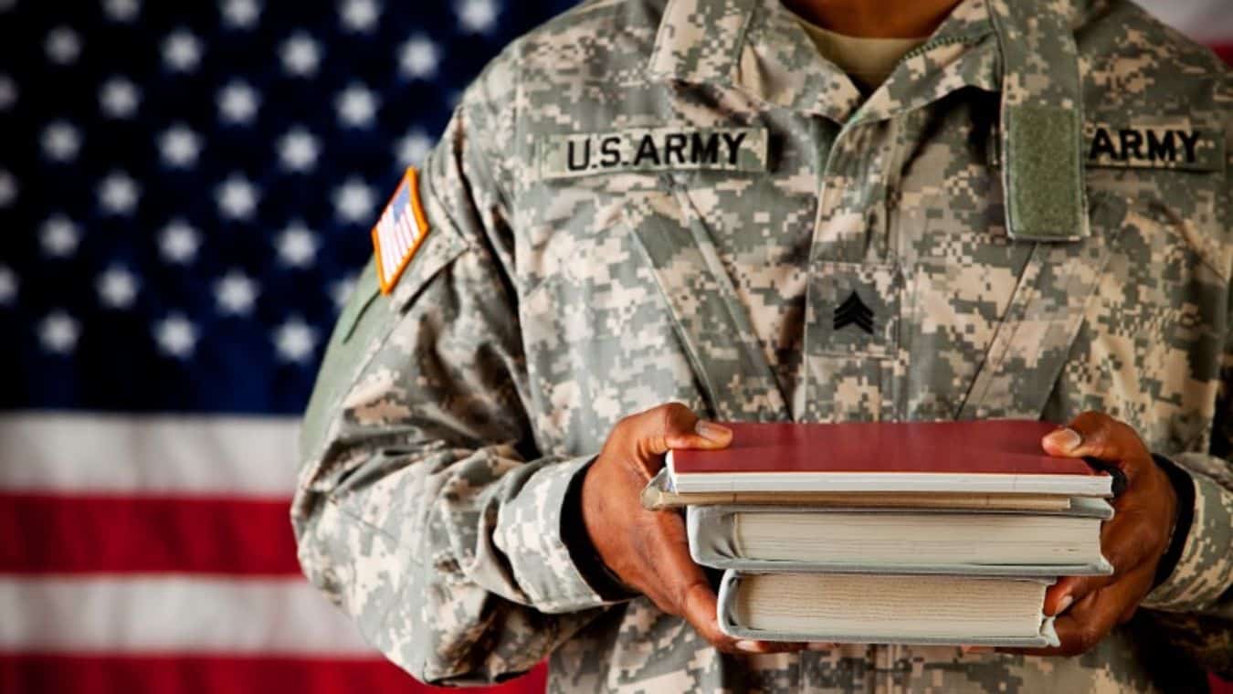 a person in military uniform holding textbooks with a an American flag in the background.