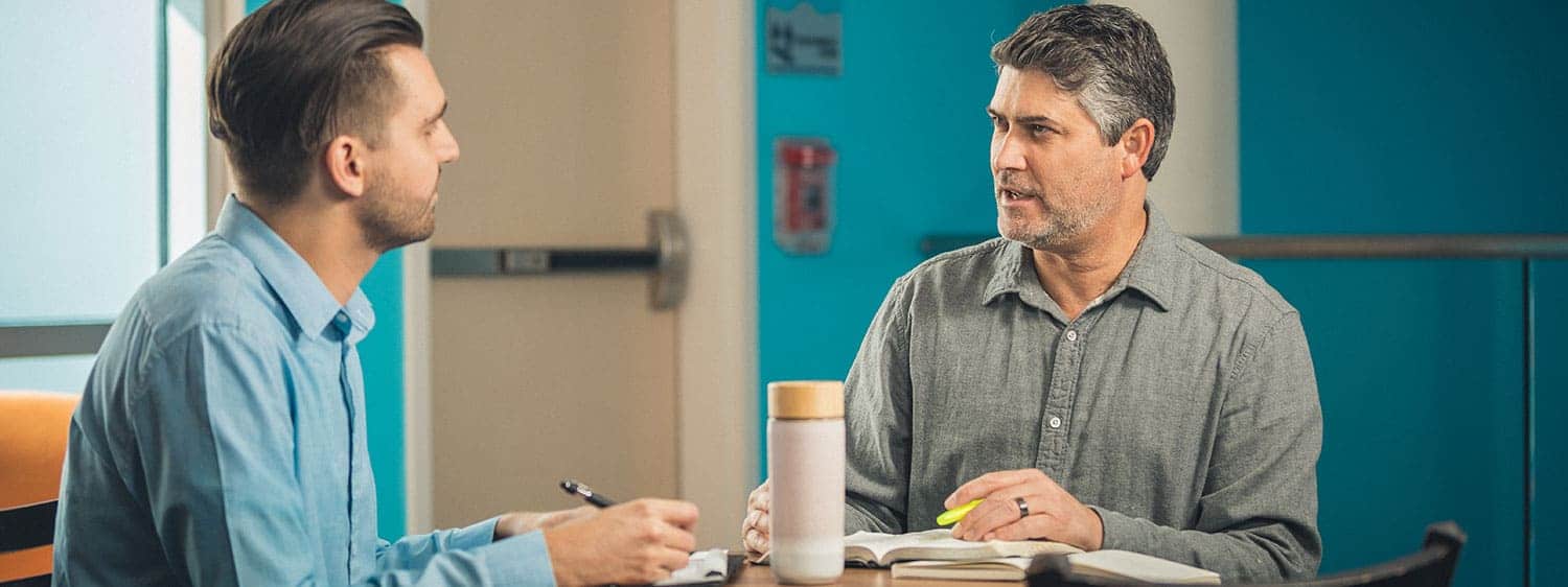 Two students in Regent's M.Div. in Theology & Ministry - Christian Discipleship program have a discussion sitting at a table together with study materials on the table.