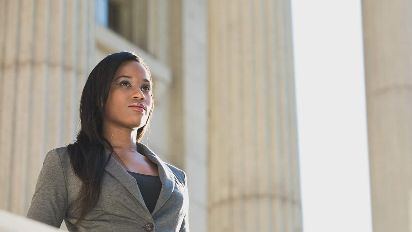 An alumna of Regent University's MAOL with an online Master's degree in Global Business Leadership & Communication wearing a gray suit standing in front of columns.