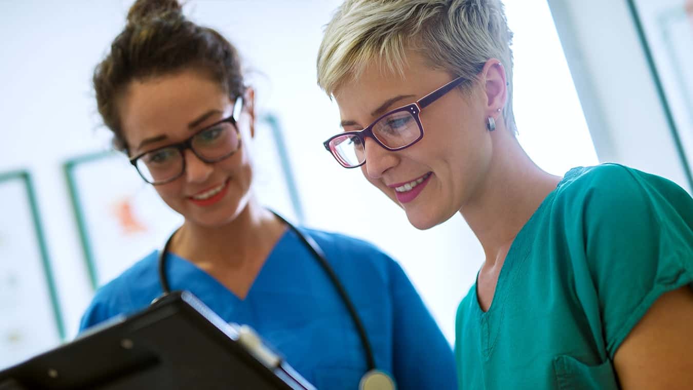 Two students in Regent's MAOL degree in Healthcare Management studying in scrubs at the premier Christian University in Virginia.