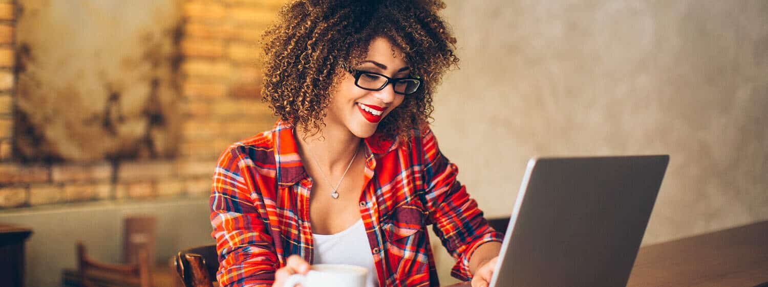 A lady smiles in front of an open laptop: Earn your eLearning certificate online at Regent University.