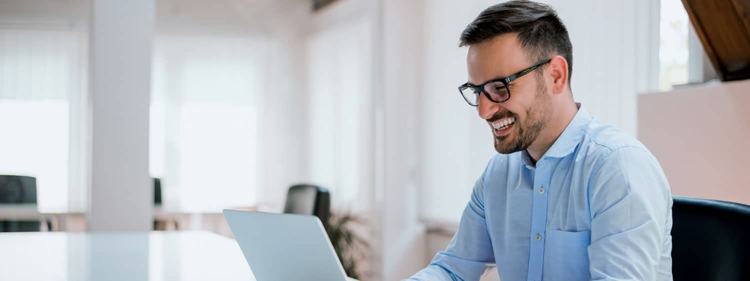 A person smiles while working on his laptop.