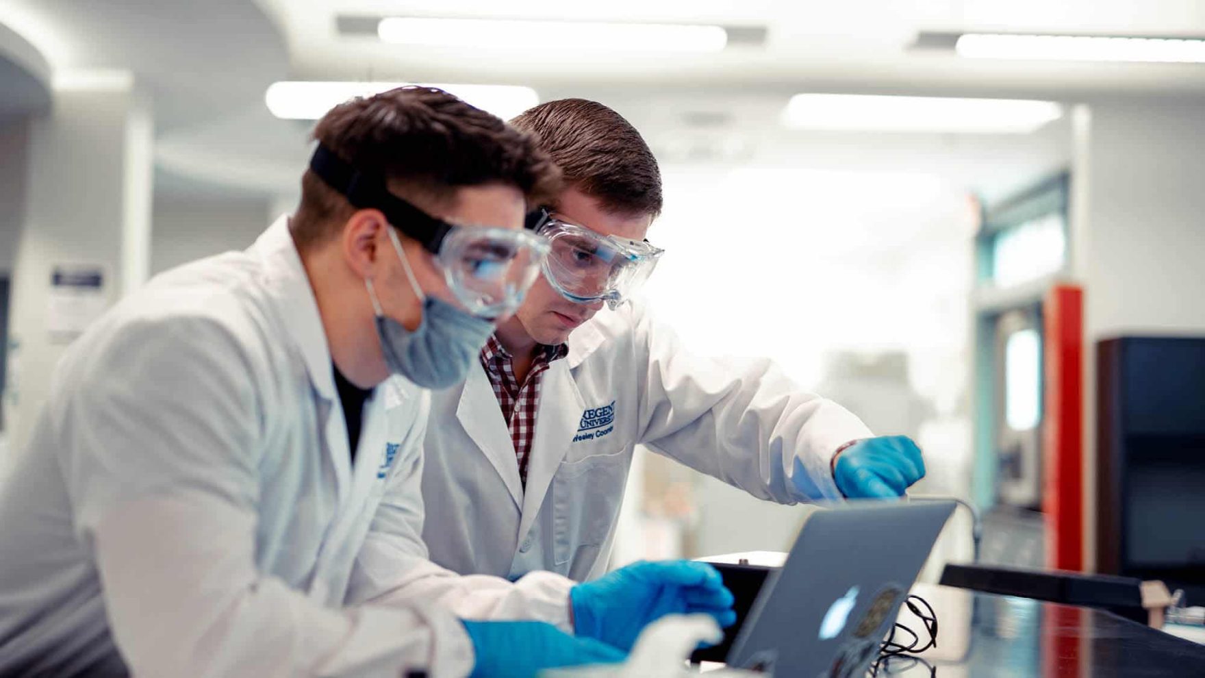 Two biology students looking at data on a laptop: Explore Regent's B.S. in Biophysical Sciences – Biology program.