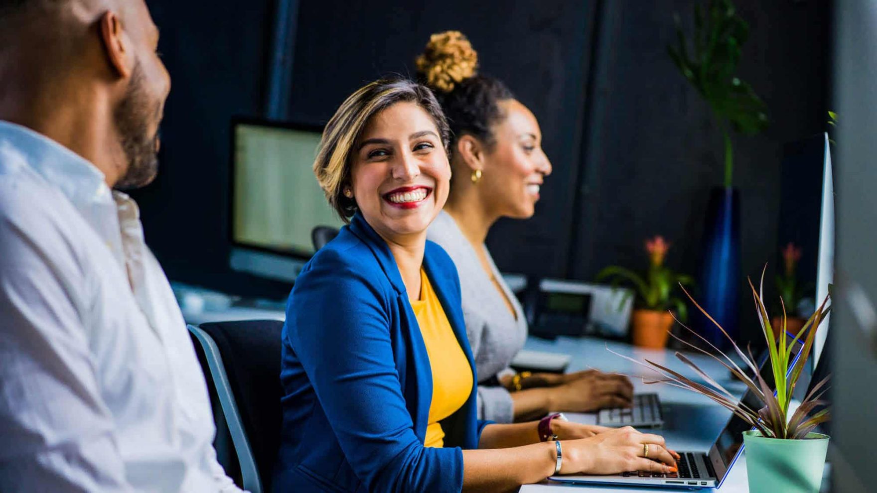 A lady smiles at her colleague while typing: Explore the communication certificate at Regent University.