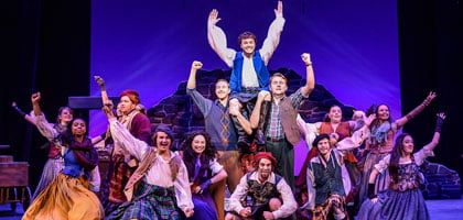 Regent University students costumed on stage end a musical number with arms in the air.