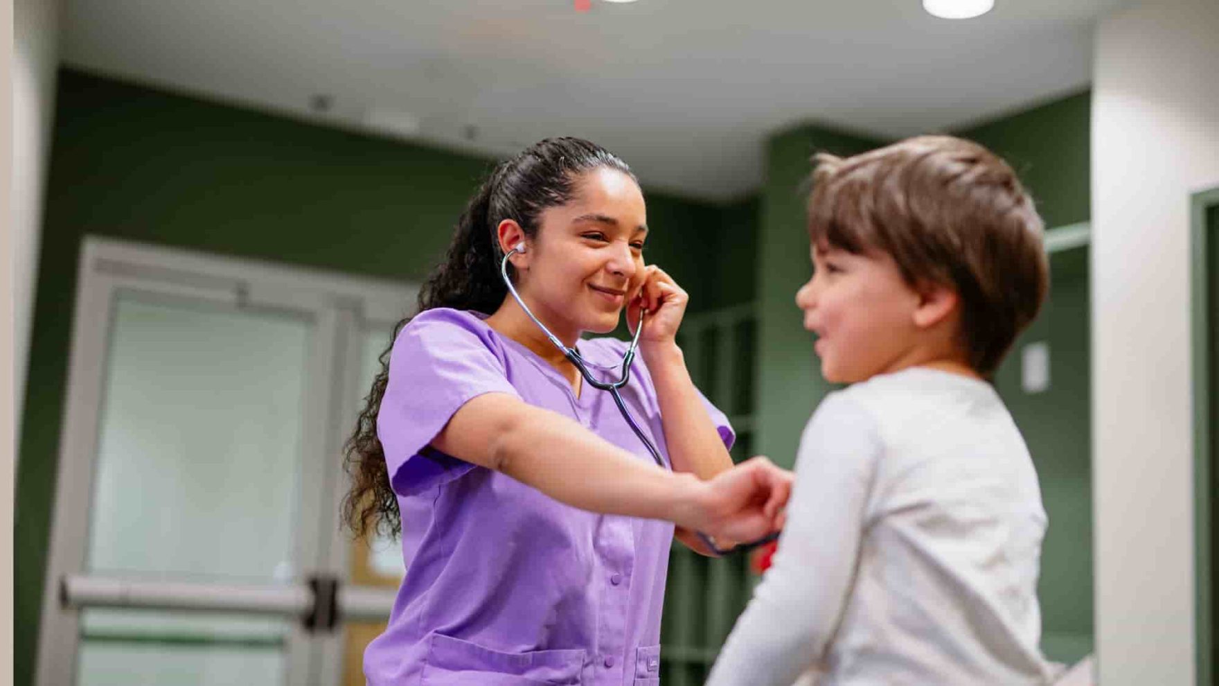 Nurse in purple scrubs checking vitals of child in a white long sleeve shirt.