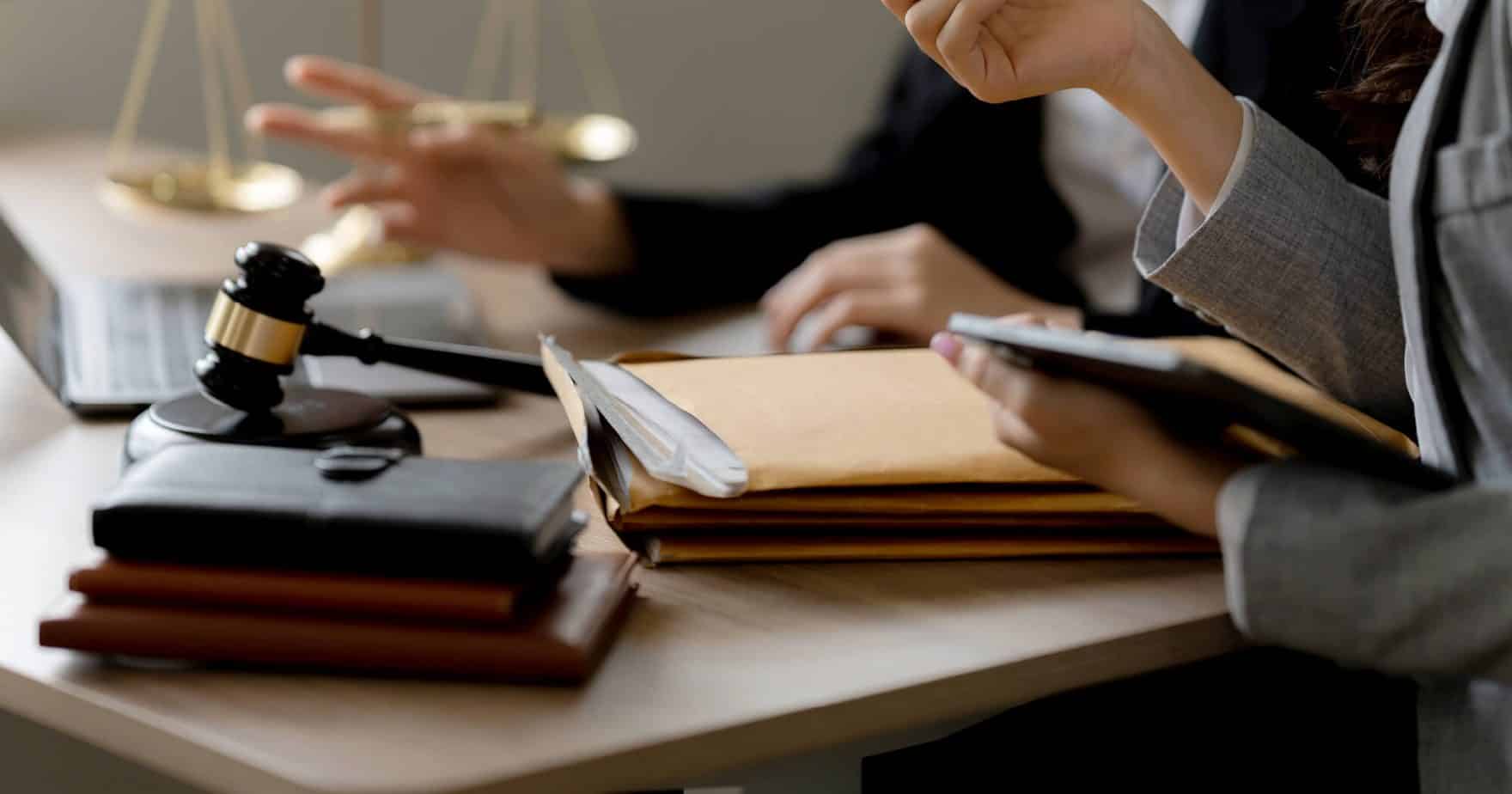 Hands of Regent University students in the Criminal Justice program working on a law desk with paperwork, notebooks, and a gavel