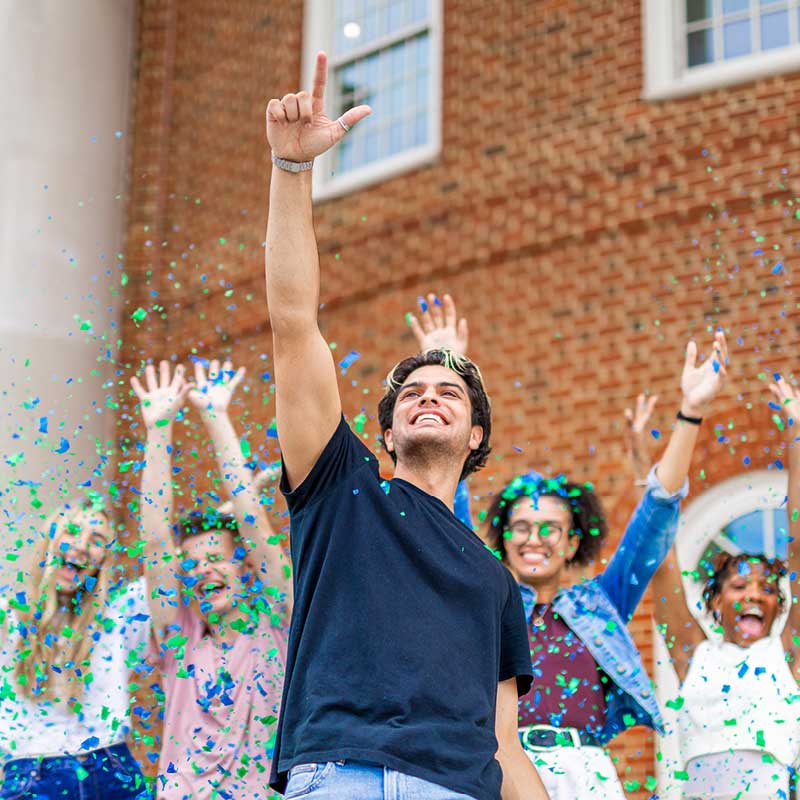 Five freshman at Regent University celebrating during Welcome Week with blue and green confetti.