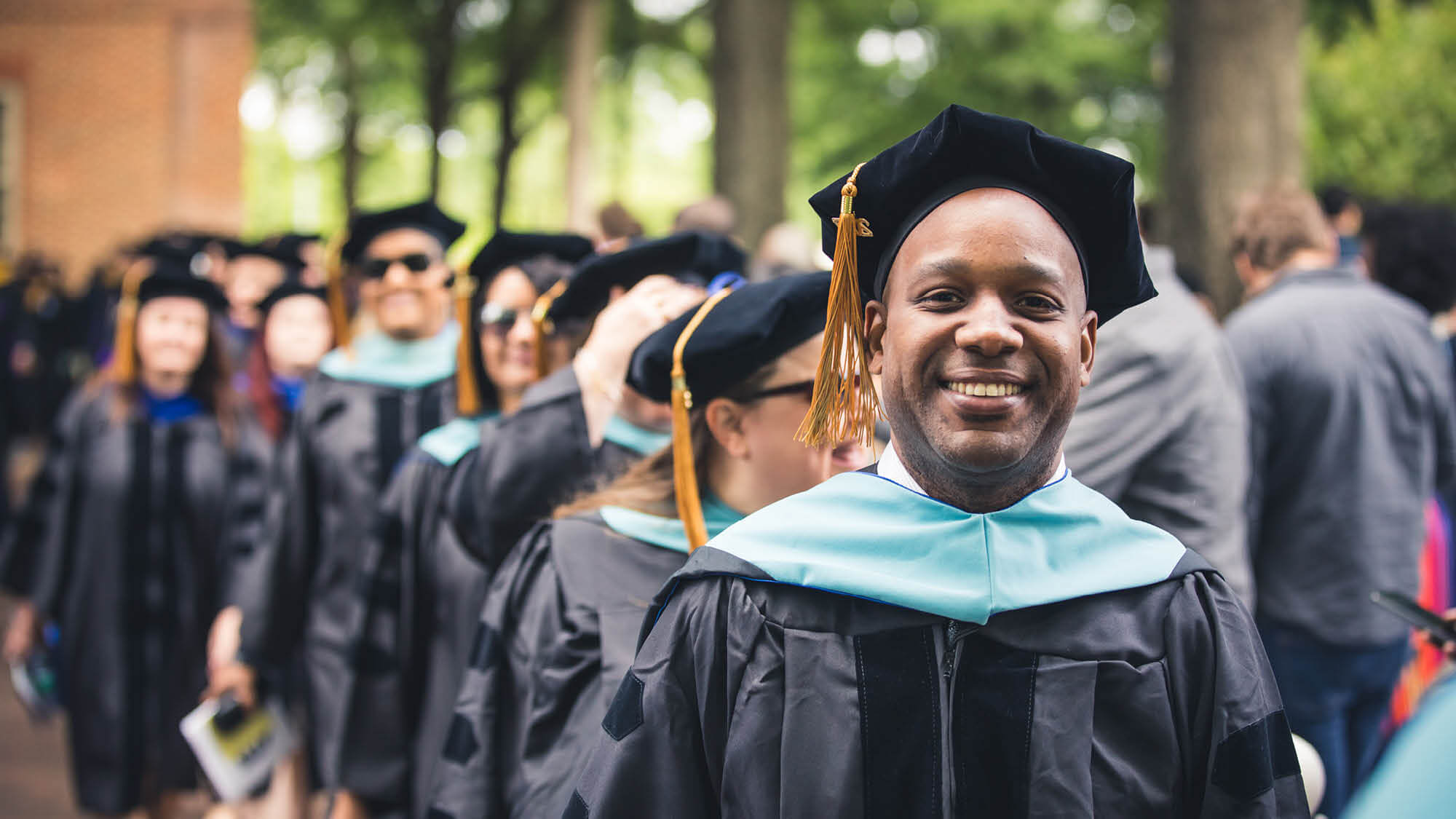 A Regent University School of Education doctoral student in graduation regalia walking and smiling on the Virginia Beach campus.