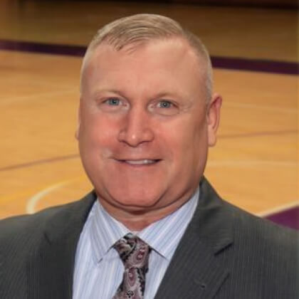 Headshot of Spencer Beaty on a basketball court who is hired as Regent University's new head coach of the men's basketball team.