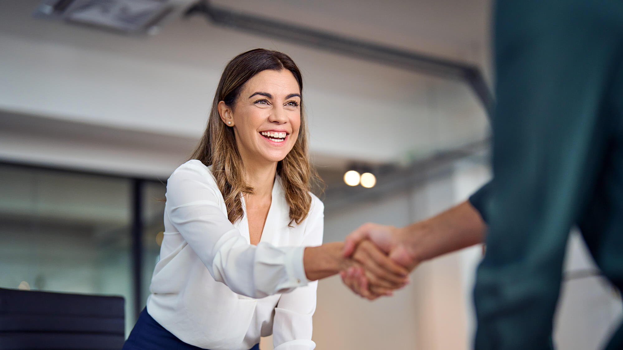 A cheerful woman shaking hands with another individual.