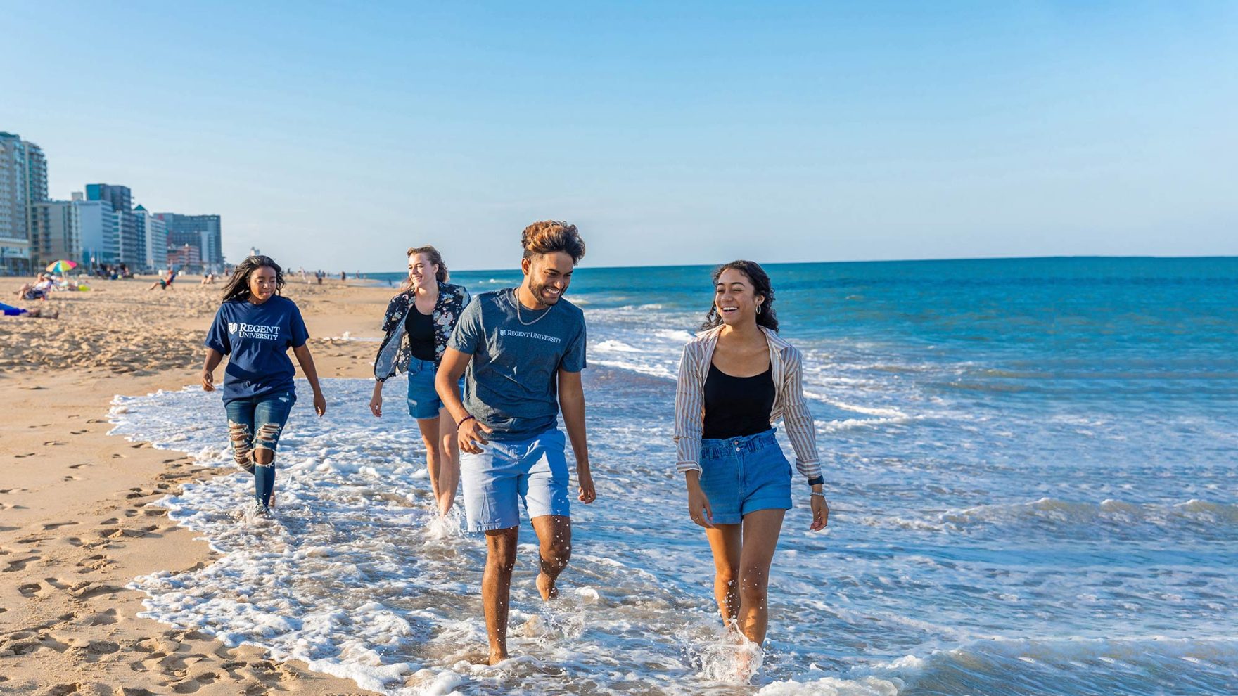 Christian college students walking on the Virginia Beach oceanfront in Regent University attire.