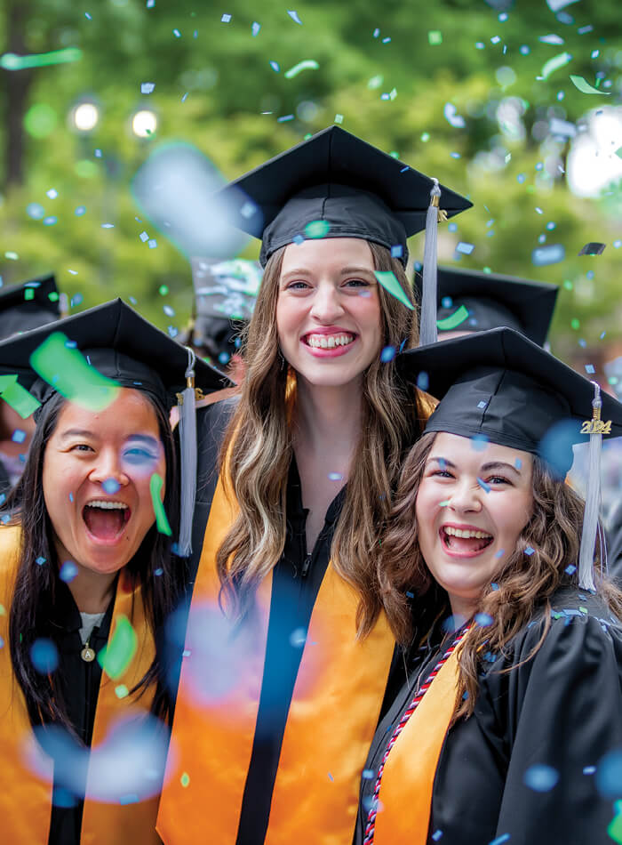 Regent University graduates smiling with confetti falling on -campus in Virginia Beach.